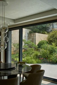A cozy dining area with a wooden table and chairs, a potted plant, and a vase, near a window allowing natural light