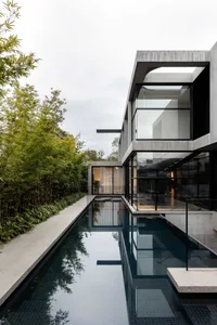 A modern house with a swimming pool in its backyard, surrounded by a fence, and featuring large windows for natural light