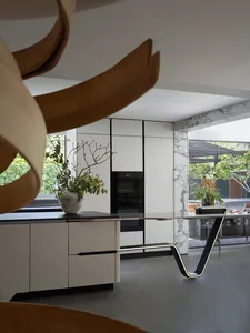 Open kitchen with white cabinets, marble countertops, potted plants, and chairs, near a sink and two ovens