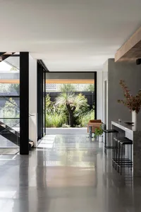 Modern open plan living area with white walls and floors, featuring a kitchen, dining room, and living room with two chairs and a dining table