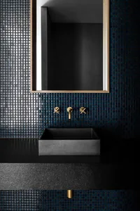 Bathroom with a sink, mirror, and black tile wall, set against a blue tile floor, creating a modern and clean atmosphere