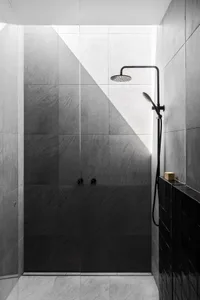 Bathroom with a corner shower, black metal pipe, and silver shower head, surrounded by tiles and featuring two knobs for water temperature or flow rate adjustment