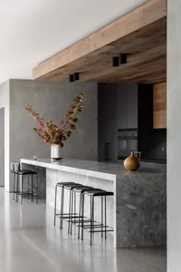 Modern kitchen with a marble island, black stools, and a large window providing natural light, featuring various appliances and a potted plant
