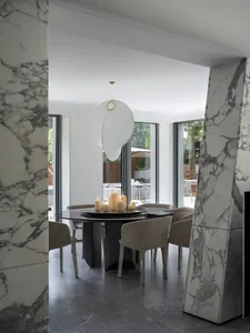 A well-lit dining space with a round table, chairs, and multiple candles, surrounded by white walls and grey floors
