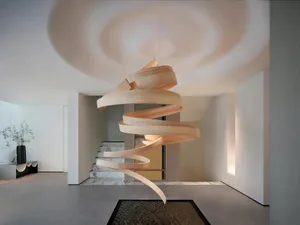 A well-lit interior space with a spiral staircase, wooden railing, and two chairs, creating a bright and inviting atmosphere