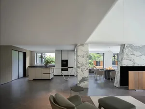 Open living area with white walls, floors, and furniture, featuring a kitchen, dining, and living space with potted plants