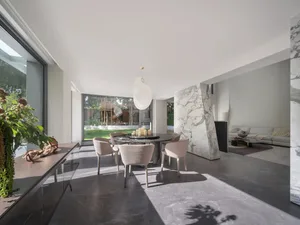 Open modern living space with a dining table, chairs, and a couch near a large window allowing natural light to fill the space