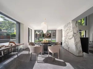 Open modern dining space with a glass-topped dining table surrounded by chairs, a kitchen area with a sink and refrigerator, and a minimalist design