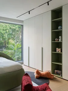 Cozy bedroom with a large bed, a chair, and two teddy bears, featuring a green theme and natural light from the window