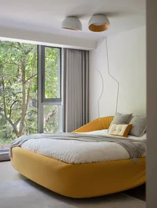 A hotel bedroom with a large yellow bed, white comforter, and orange mattress, featuring two pillows and a window with natural light