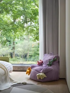 Cozy bedroom with a purple chair, wooden floor, and stuffed animals, featuring a warm and inviting atmosphere