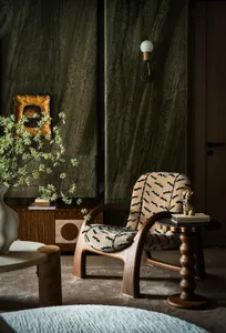 Cozy interior space with a wooden chair, black and white striped chair, stone wall, vases, and a book, featuring natural materials and inviting atmosphere