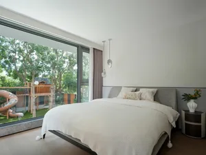 A well-lit bedroom with a large white bed, two smaller beds, and natural sunlight coming through the window