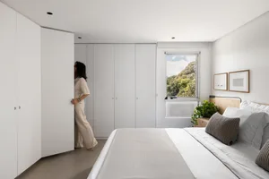A bedroom with a white bed, two dressers, and a potted plant, creating a clean and organized atmosphere