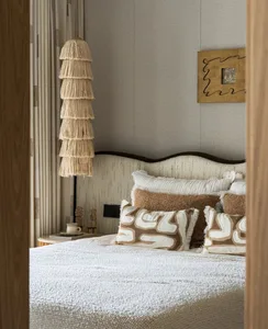 Cozy bedroom with a white bed, brown pillows, a wicker lamp, and a standard lamp, a chair, and a dining table