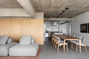 Open concept living area with a modern and minimalistic design, featuring a couch, wooden dining table, refrigerators, and neutral tones