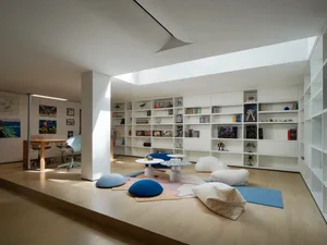 Open living area with white walls, wooden floors, bookshelves, chairs, couches, and a dining table in a modern and cozy atmosphere