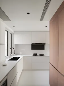 A modern kitchen with white cabinets, countertops, and two sinks, featuring a black oven and a clean design