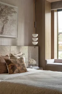 Cozy bedroom with a large bed, brown pillows, and a bench, featuring two vases and a white sheet