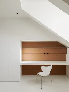 A clean and organized white room with wooden accents, featuring a desk, chairs, and decorative objects