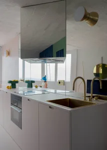A modern kitchen with white cabinets, a large mirror above the sink, and fruits such as apples and oranges on the countertop