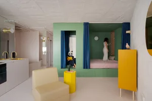 Cozy bedroom with green walls, yellow accents, two beds, a chair, a couch, and a person standing in the middle of the room
