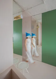 Two women walk down a hallway with a green wall, mirror, and chairs, creating a unique and artistic space