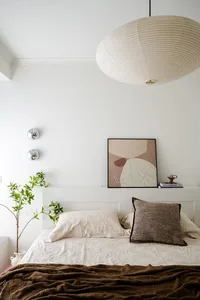 A calm bedroom with a white bed, two potted plants, and a clock on the wall