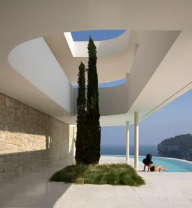 Modern house with a large glass wall overlooking a pool area, featuring white walls and a curved roof, with two people in a relaxed atmosphere
