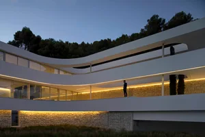 A modern building with curved walls and a stone facade, featuring multiple windows and a contemporary design