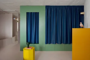A serene interior space with a green wall, blue curtains, and a yellow table, creating a calm and inviting atmosphere