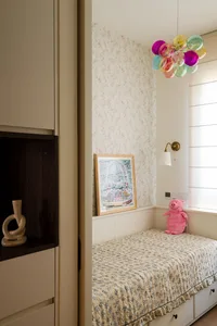 A small bedroom with a bed, pink blanket, and two teddy bears, surrounded by floral-patterned walls creating a cozy atmosphere