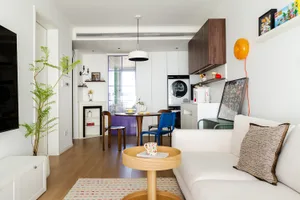 Modern living room, kitchen, and dining area with white walls, a couch, refrigerator, oven, sink, and dining table