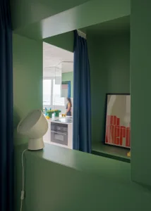 A woman stands in front of a double sink in a green kitchen with a refrigerator and oven, surrounded by a cozy atmosphere
