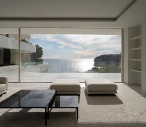 Open living area with two white couches in front of large windows offering ocean views, surrounded by modern home design with clean lines and minimal decoration