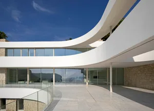 A large, well-lit modern building with curved walls, glass windows, white walls, and a combination of stone and glass elements, allowing for ample natural light to enter the space