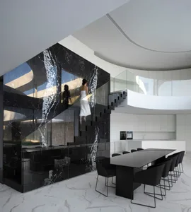 Modern open concept living space with a large black dining table, chairs, and a kitchen area with a refrigerator, featuring two people in a functional and design-focused atmosphere