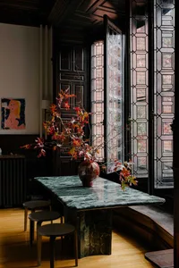 Dining room with a marble table, vase of flowers, and natural light from a window, surrounded by chairs in an elegant and sophisticated space