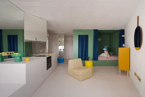 Open living space with green walls, white floors, and modern furniture, featuring a couch, chair, clocks, and decorative objects