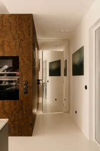 A clean and bright hallway with white walls and flooring, featuring three framed pictures and a microwave near one of the doors