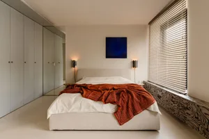 Cozy bedroom with a large white bed, red blanket, and natural light from a window, accompanied by two lamps for additional lighting