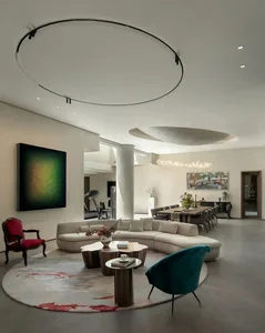 A well-lit living room with a large couch, chairs, dining table, and potted plants, set in a modern home with natural sunlight coming through windows