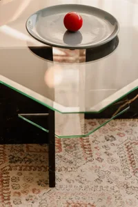 Cozy living space with a glass coffee table on a rugged carpet, featuring a vase and two bowls, creating a warm and inviting atmosphere