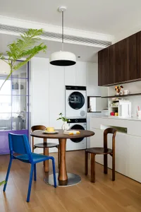 Modern kitchen with wooden floors, white cabinets, a dining table, chairs, and a potted plant, with a clean and organized atmosphere