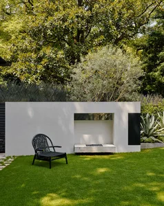 A serene outdoor living area with a white fireplace in a grassy field, surrounded by two chairs for relaxation and socializing