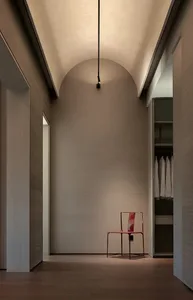 A minimalist hallway with a red chair in the center, surrounded by white walls and a single light source casting a shadow on the wall