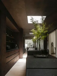 Modern kitchen with dark wood cabinets, granite countertops, and black appliances, featuring two sinks, a refrigerator, and a dining table with chairs