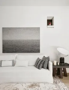 Cozy modern living space with white walls, a lamp, and decorative items, featuring a large painting and a chair, with soft lighting and candles
