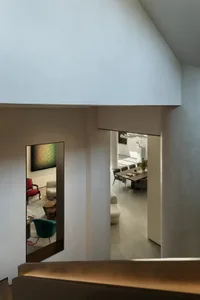 Open living area with white walls, a couch, chairs, dining table, and decorative vase, set against a clean and minimalist background