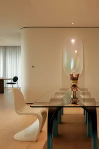 A modern dining space with a glass table surrounded by chairs in a symmetrical arrangement, creating a clean and minimalist ambiance